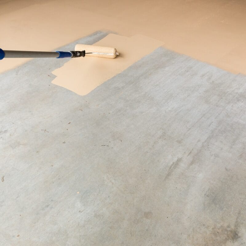 Worker Painting Floor of Garage with Roller.